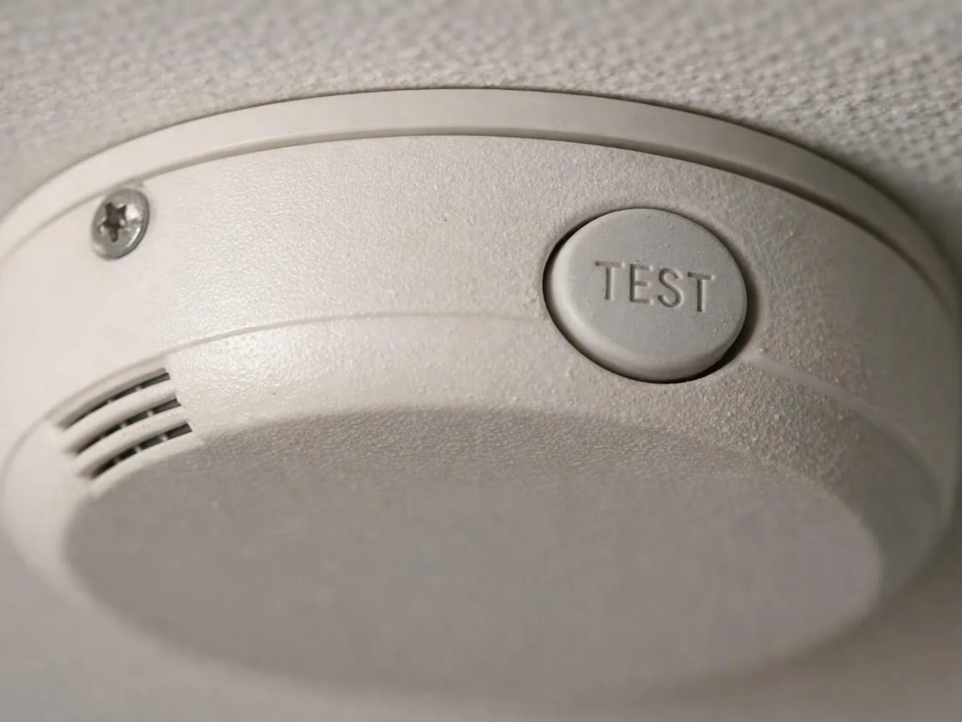 A ceiling smoke detector with a TEST button is mounted against a textured ceiling