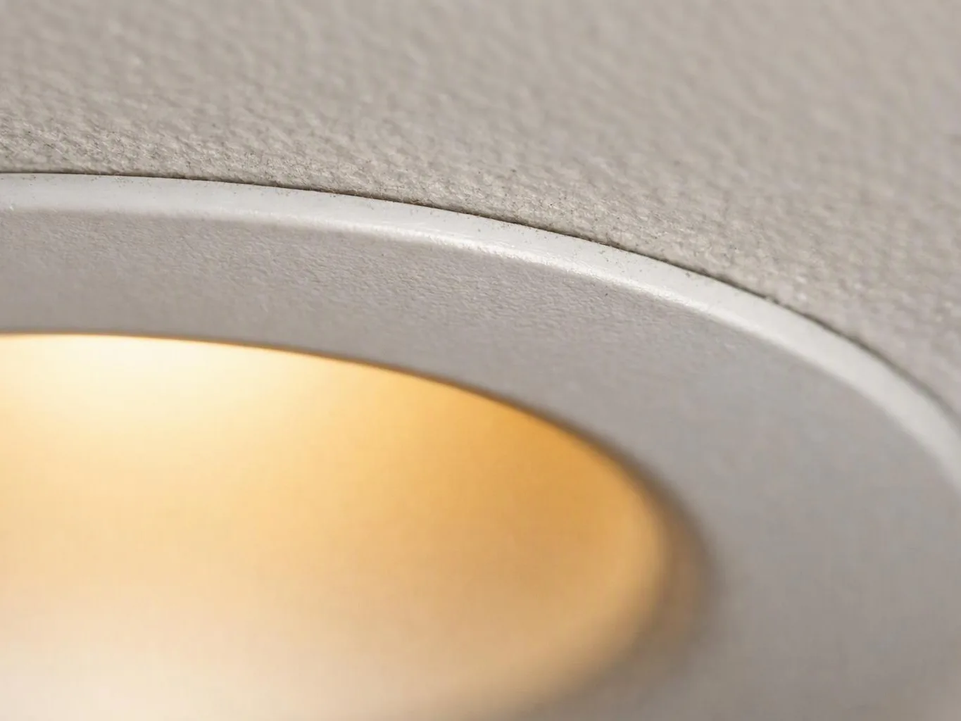 Close-up of a ceiling light with a glowing circular diffuser set in a textured gray fixture