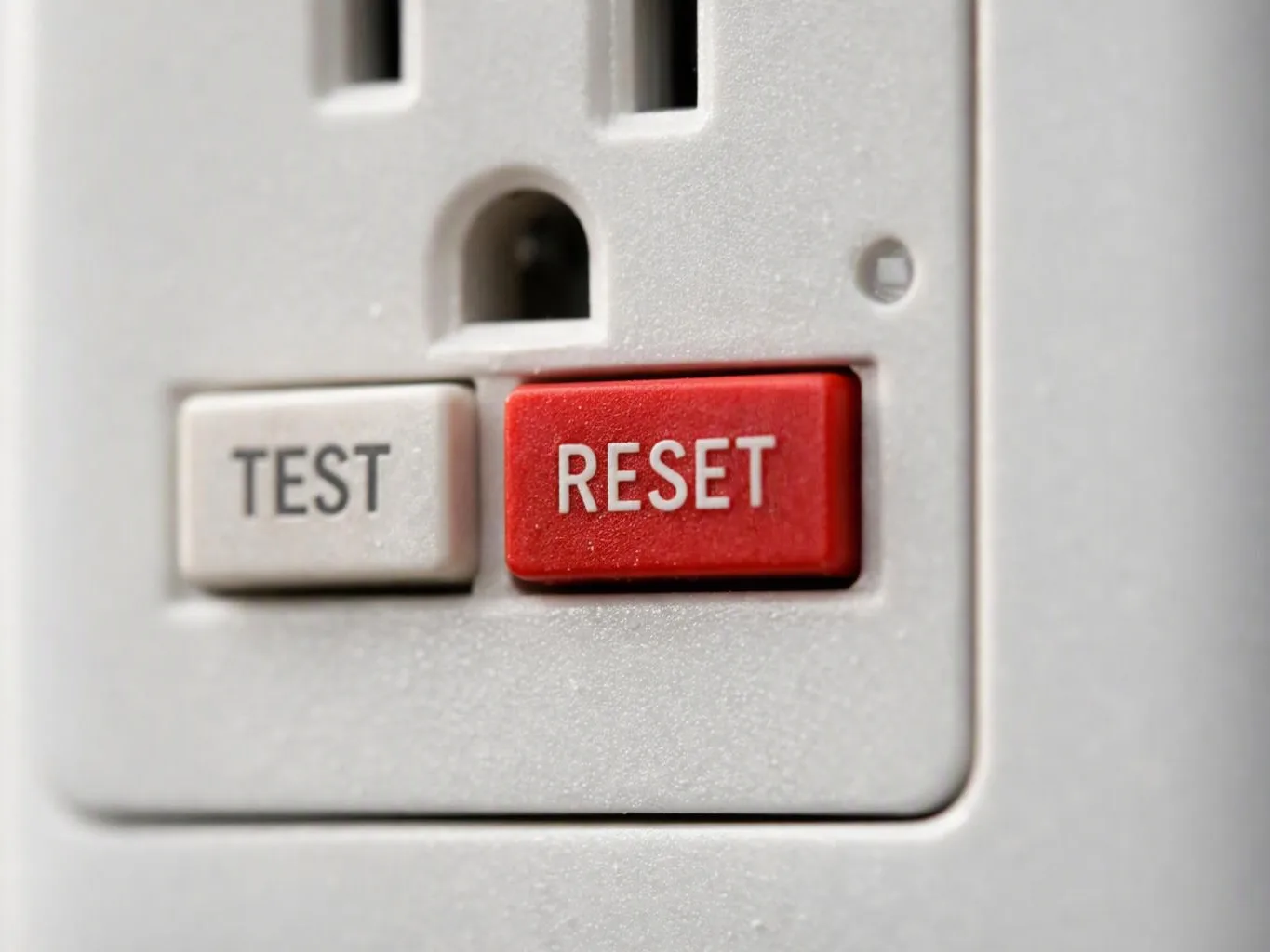 Close-up of an electrical outlet with white TEST and red RESET buttons on a wall plate
