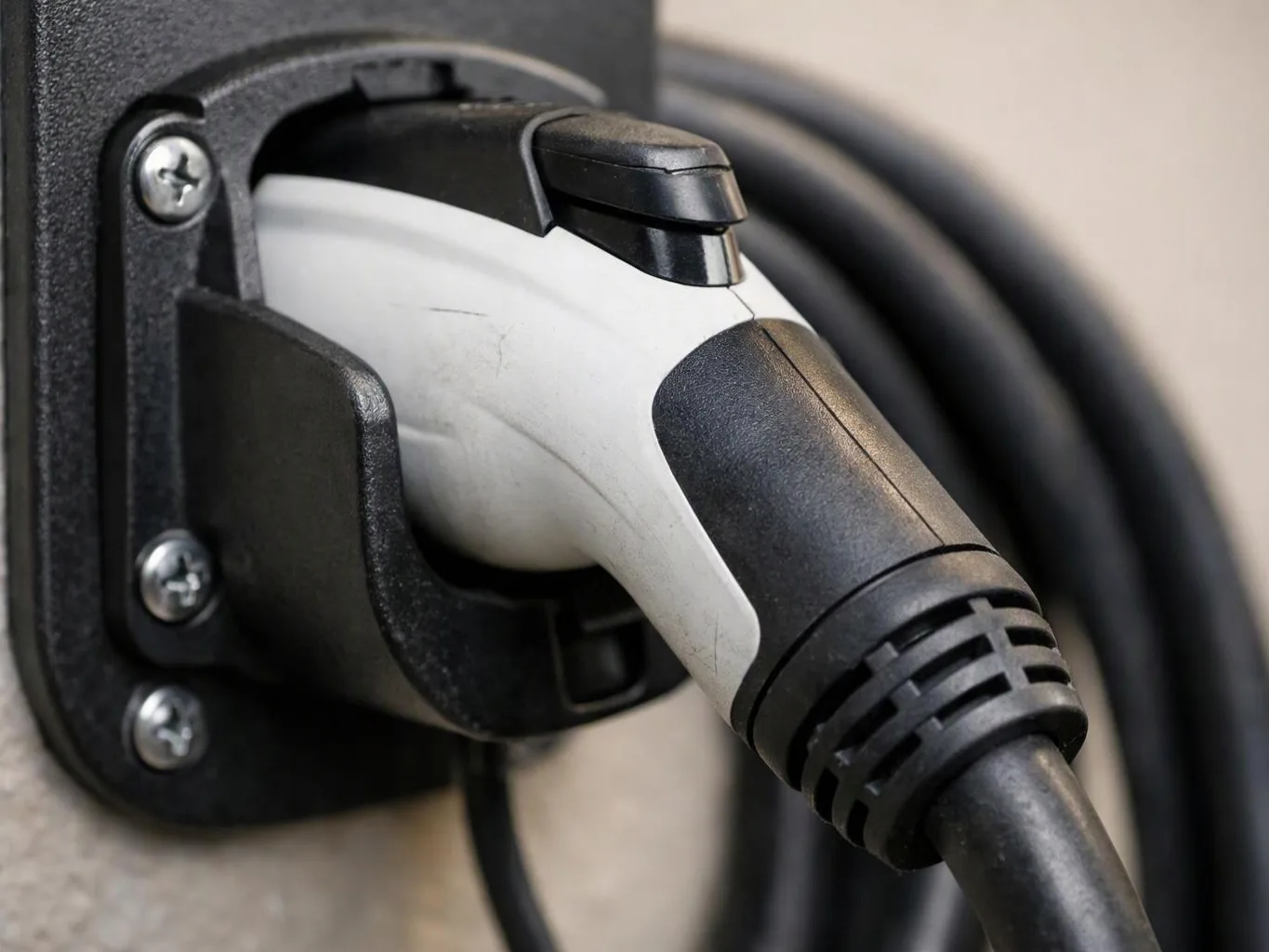 A close-up shows an electric vehicle charging plug inserted into a wall-mounted charging port with a coiled cable